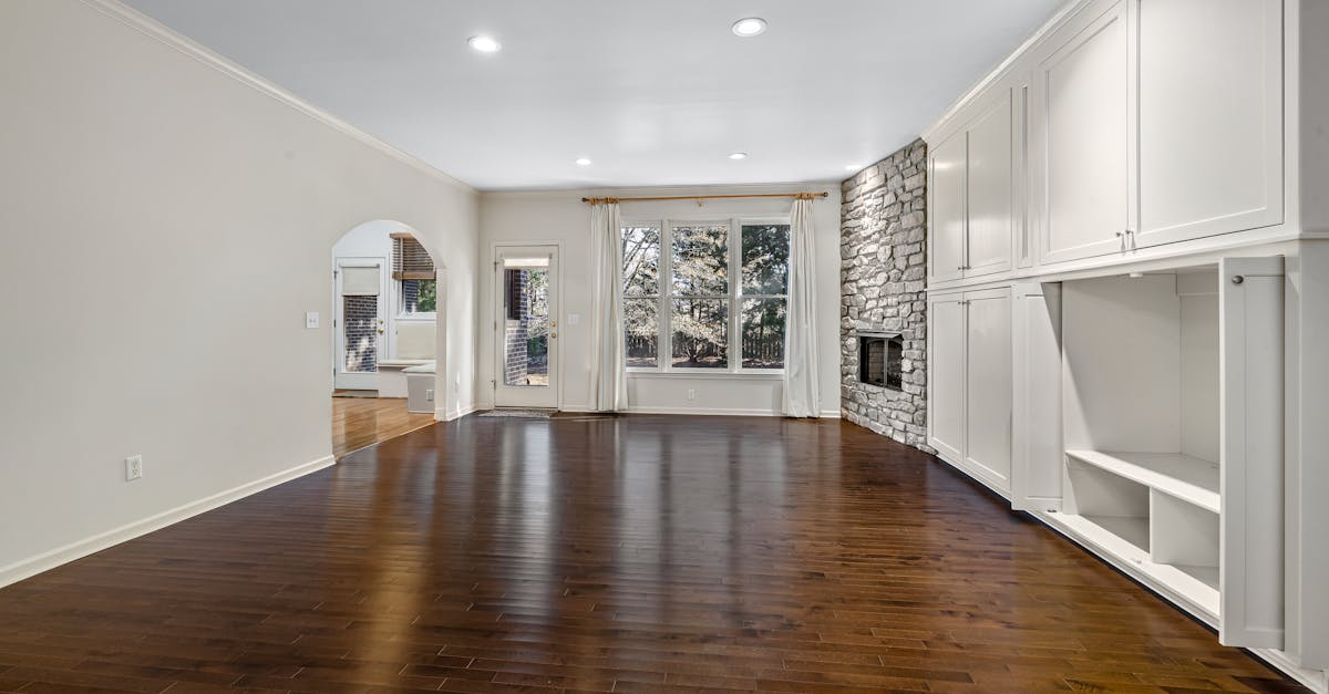 Bright, empty living room featuring hardwood floors and stone fireplace.